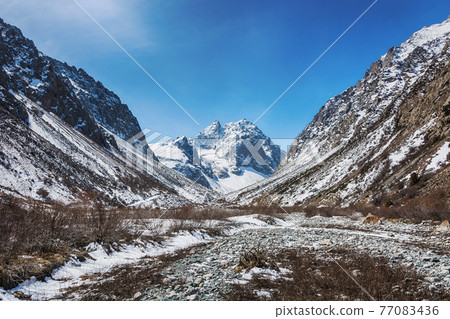 Idyllic winter landscape with hiking trail in the mountains. Rocks, snow and stones in mountain valley view. Mountain panorama. 77083436