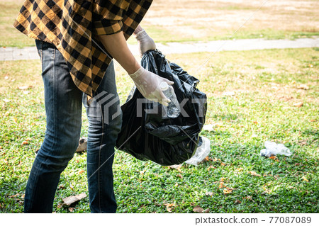 Volunteer man in gloves to picking up plastic bottle into plastic black bag for cleaning the park Volunteer man in gloves to picking up plastic bottle into plastic black bag for cleaning the park 77087089