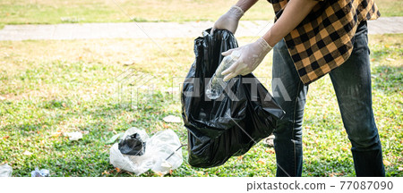 Volunteer man in gloves to picking up plastic bottle into plastic black bag for cleaning the park Volunteer man in gloves to picking up plastic bottle into plastic black bag for cleaning the park 77087090