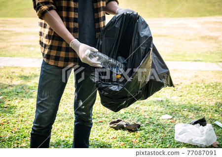 Volunteer man in gloves to picking up plastic bottle into plastic black bag for cleaning the park Volunteer man in gloves to picking up plastic bottle into plastic black bag for cleaning the park 77087091