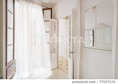 White waving curtain in empty room of refurbished apartment in Barcelona. Classic style interior with window and mirror. 77087224