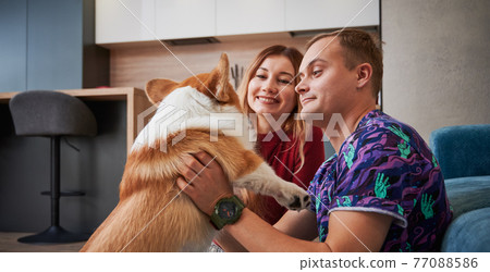Happy couple spending time with cute Corgi at home. 77088586