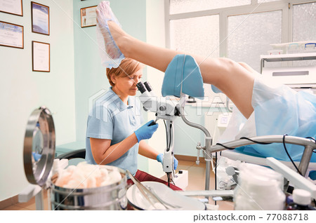 Highly qualified doctor examining woman with colposcope. 77088718
