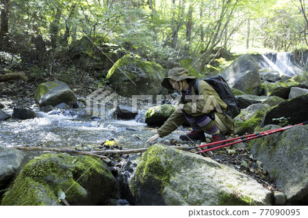 Trekking image of a young woman touching the water of the river 77090095