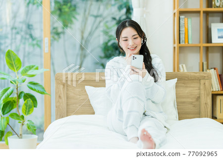 Young woman looking at a smartphone in the bedroom 77092965