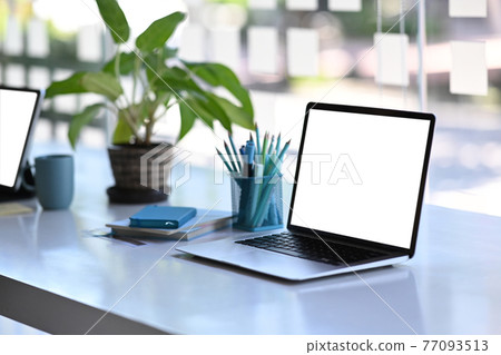 Freelancer or designer workspace with a laptop computer with blank screen, stationery and notebook on white table. 77093513