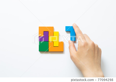 Set of color blocks puzzle pieces and hand holding last one piece on white background. Creative thinking, idea, problem solving, success concept. top view 77094298