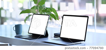 Modern workspace with laptop computer and digital tablet on white desk. Blank screen for graphics display montage. Modern workspace with laptop computer and digital tablet on white desk. Blank screen for graphics display montage. 77094780