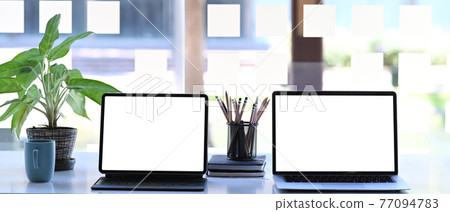 Front view of laptop computer and digital tablet on creative workspace. Blank screen for graphics display montage. Front view of laptop computer and digital tablet on creative workspace. Blank screen for graphics display montage. 77094783