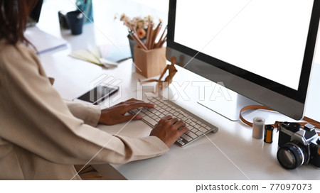 Young female photographer hands typing on keyboard while sitting in front of computer at creative workspace. Young female photographer hands typing on keyboard while sitting in front of computer at creative workspace. 77097073