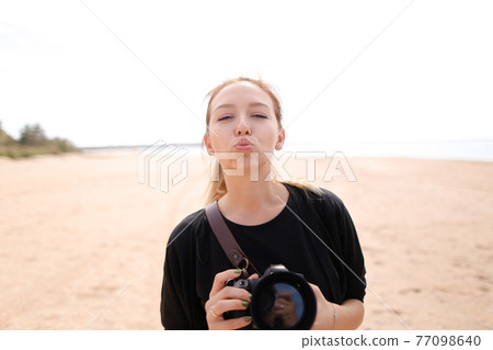 Portrait of young woman with camera on beach. 77098640