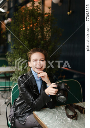 Young happy woman sitting at street cafe with camera. Young happy woman sitting at street cafe with camera. 77098823