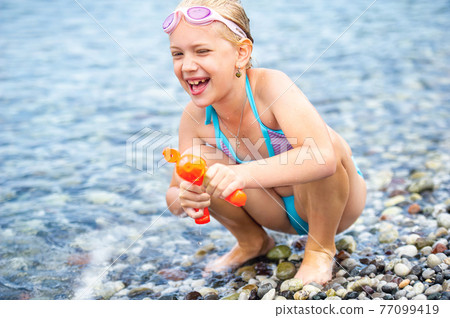 Adorable little girl swims in the sea and plays with a water gun on a beach in Turkey 77099419