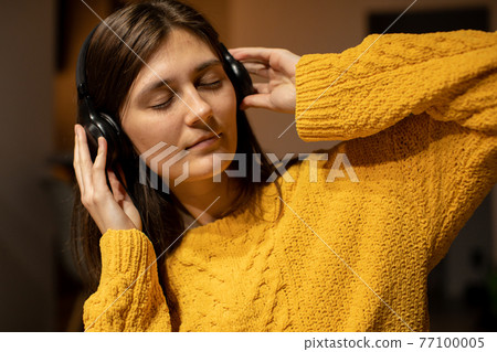 girl In yellow casual sweater closed eyes enjoys to music with headphones 77100005