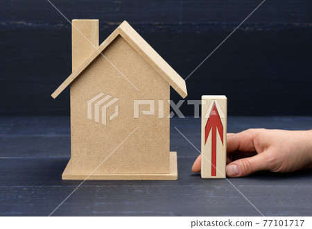 wooden house and a female hand holds a bar with a red arrow. Real estate value increase concept 77101717