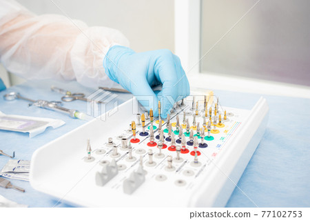 set of instruments for dental implantation on the table at the dentist. Doctor in blue gloves chooses an instrument 77102753
