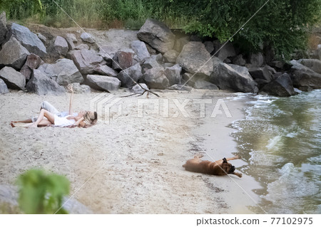 A couple of lovers lies on the beach next to their dog. Camping with pets. Love concept for each other and animals 77102975
