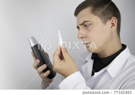 A lab technician examines a sample of shampoo he was given for analysis. Chemical analysis of the composition of detergents, shampoos and hair conditioners. Laboratory research concept. 77102985
