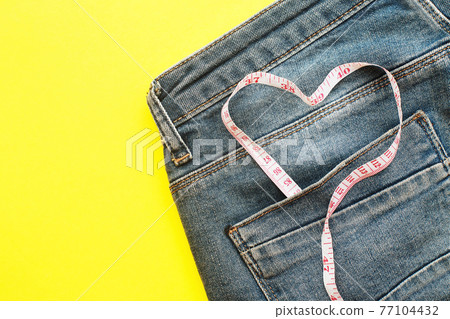 blue jeans with measure tape in pocket in form of a heart. concept of healthy lifestyle and diet with love to your body blue jeans with measure tape in pocket in form of a heart. concept of healthy lifestyle and diet with love to your body 77104432