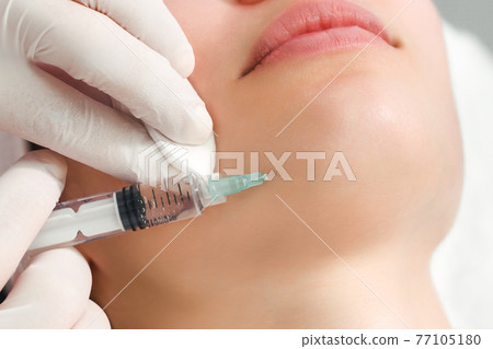 The doctor cosmetologist makes the rejuvenating facial injections procedure for tightening and smoothing wrinkles on the face skin of a beautiful, young woman in a beauty salon. Cosmetology, skincare The doctor cosmetologist makes the rejuvenating facial injections procedure for tightening and smoothing wrinkles on the face skin of a beautiful, young woman in a beauty salon. Cosmetology, skincare 77105180