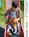 A 3-year-old boy playing with his grandma on a park slide 77105267