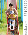 A 3-year-old boy playing with his grandma on a park slide 77105270