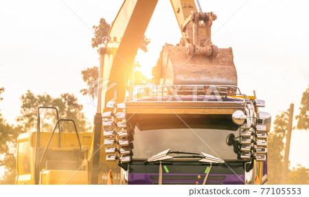 Backhoe working by digging soil at construction site and loading to the truck. Bucket of backhoe transport soil to truck. Crawler excavator dump dirt soil to heavy dump truck. Excavating machine. 77105553
