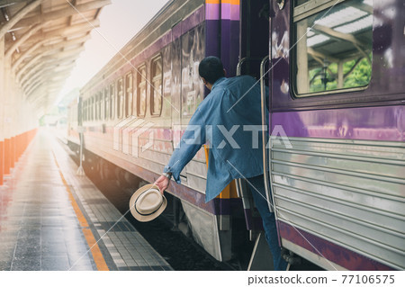 A man with hat holding handrail in train at the open door. People travel local transport. A man with hat holding handrail in train at the open door. People travel local transport. 77106575