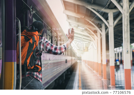 A man grabbed the handrail of the train door and waved his hand. People travel by local transport. 77106576