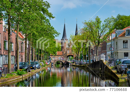 Delft cityscape view with Eastern Gate Oostport and canal with cars and bicycles parked along 77106688