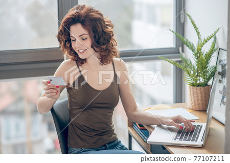 Dark-haired pretty woman holding a credit card and planning to make online payments 77107211