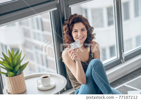 Dark-haired pretty woman holding a credit card and planning to make online payments Dark-haired pretty woman holding a credit card and planning to make online payments 77107212