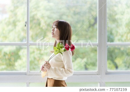 A young woman holding two roses by the window A young woman holding two roses by the window 77107239