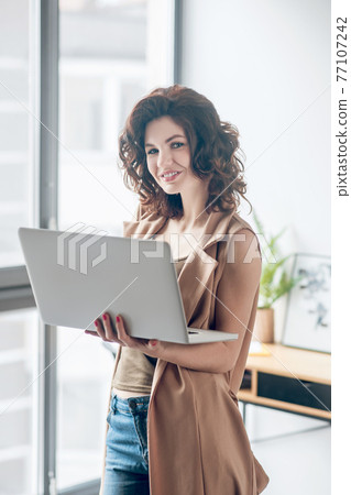 Dark-haired pretty woman working on a laptop and looking contented 77107242