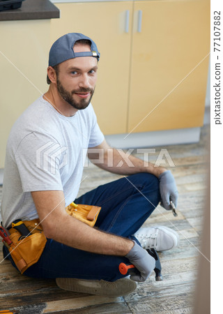 Full length shot of young repairman looking at camera, holding plumbing tools in his hands while sitting in Lotus pose on the floor indoors 77107882