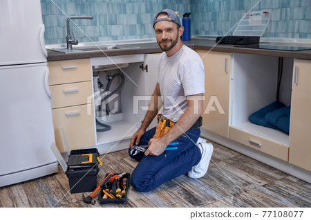 Young caucasian male worker on floor next to kitchen sink 77108077