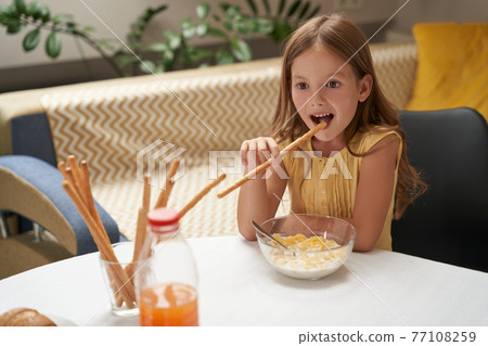 Cute little caucasian girl having breakfast at home and smiling, eating cereals with milk and snacks Cute little caucasian girl having breakfast at home and smiling, eating cereals with milk and snacks 77108259