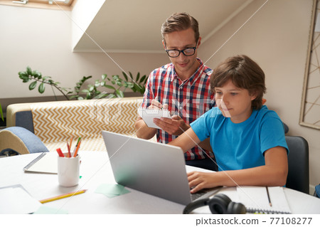 Homeschooling concept. Young father wearing eyeglasses and his little son watching video lesson online, man making some notes 77108277