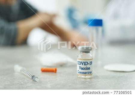 Coronavirus vaccine and medical syringe on table in clinic Coronavirus vaccine and medical syringe on table in clinic 77108501