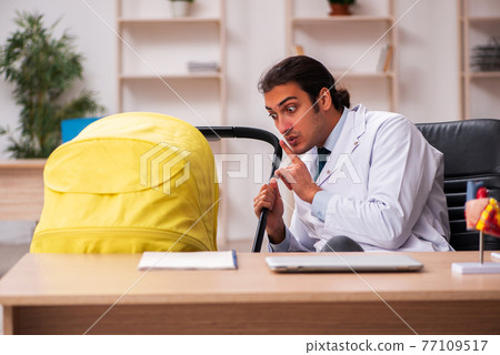 Young male doctor looking after new born in the clinic Young male doctor looking after new born in the clinic 77109517
