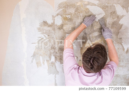 Caucasian man tearing off old wallpaper from wall preparing for home redecoration 77109599