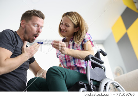 Joyful woman in wheelchair shows surprised man pregnancy test 77109766