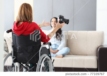 Woman in wheelchair holds camera and takes photo of model Woman in wheelchair holds camera and takes photo of model 77109767