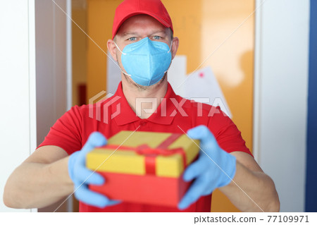 Male courier in protective mask and gloves delivers gift box 77109971