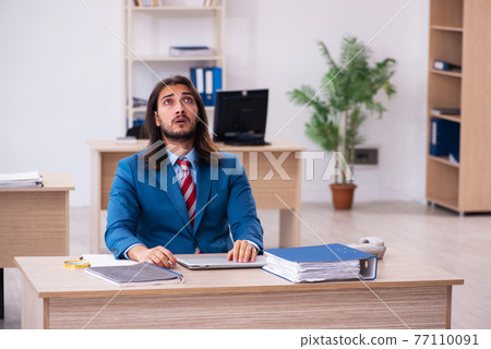 Young male employee working at workplace 77110091