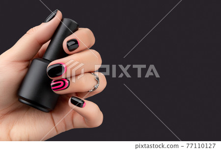 Womans hand with trendy manicure holding nail varnish on pink background Womans hand with trendy manicure holding nail varnish on pink background 77110127