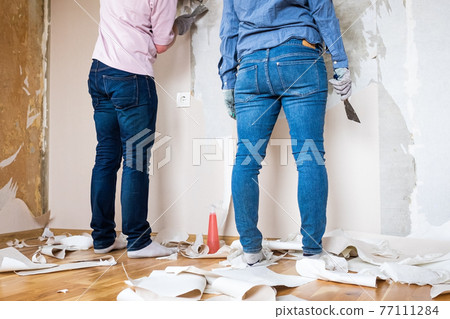 Young couple removing old wallpaper from walls preparing for flat renovation. 77111284