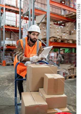 Bearded warehouse worker examining papers Bearded warehouse worker examining papers 77112768