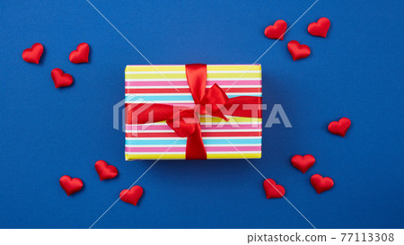 wrapped gift box with red ribbon and hearts on blue background 77113308