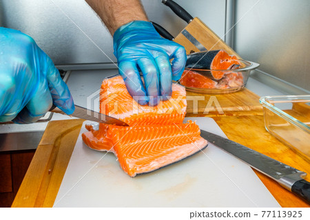The hands of the cook separate the salmon fillets from the bones with a knife. The hands of the cook separate the salmon fillets from the bones with a knife. 77113925